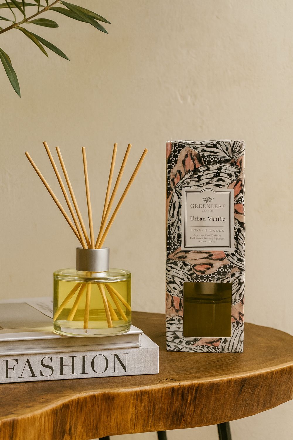 Greenleaf Urban Vanille Reed Diffuser mit 8 Holzstäbchen in einem Glasfläschchen neben seiner Verpackung, auf einem Holztisch.