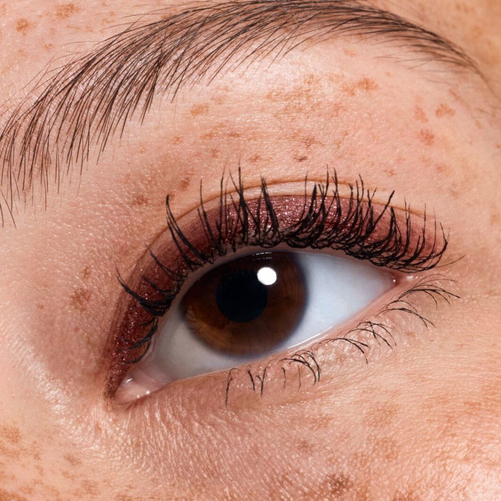 Nahaufnahme eines Auges mit Sommersprossen. Rotes Augen-Make-up. Lange Wimpern.