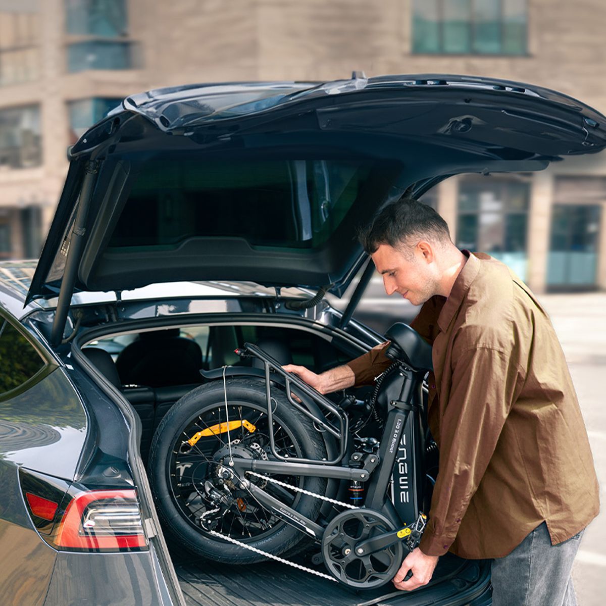 Mann entnimmt ein zusammengeklapptes schwarzes Elektrofahrrad aus einem Auto. Das ENGWE-Logo ist sichtbar.