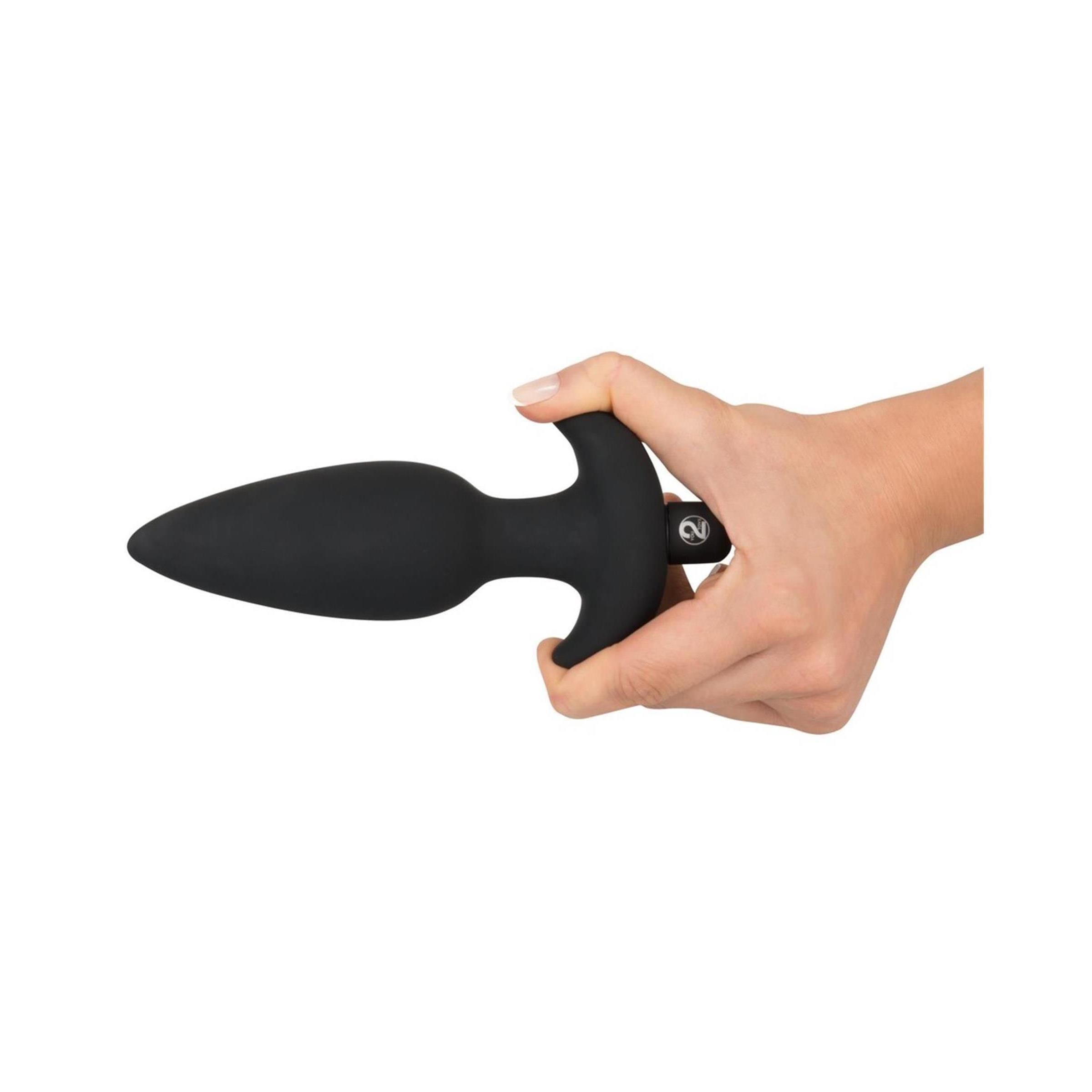 Hand hält schwarzen Analplug. Der Plug hat eine konische Form, einen T-förmigen Griff und eine Basis.