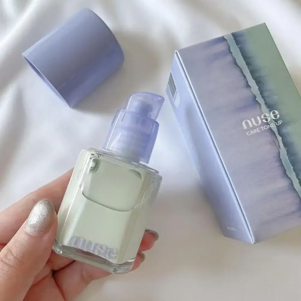 Make-up-Grundierung in Flasche und Verpackung. Flasche mit lila Deckel, grüne Flüssigkeit. Marke 'nuse'.