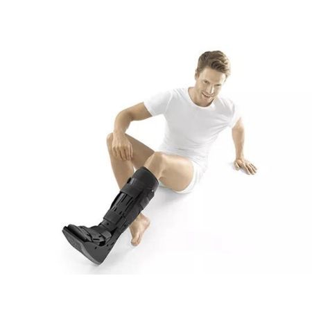 Mann sitzt mit schwarzem Air Walker am Bein. Klettverschlüsse und Kunststoffschale sichtbar.