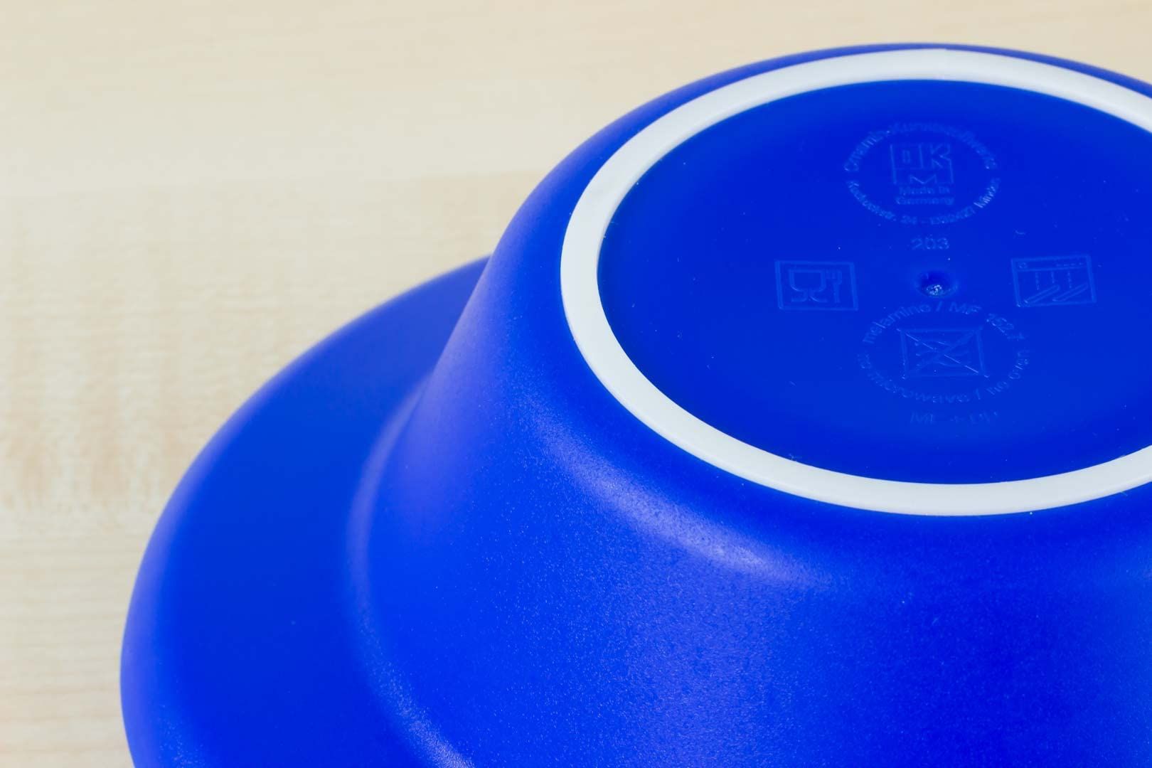 Blaue Thermoschale, Unterseite. Blaue Farbe, weißer Rand. Symbole für Pflegehinweise. Runde Form.