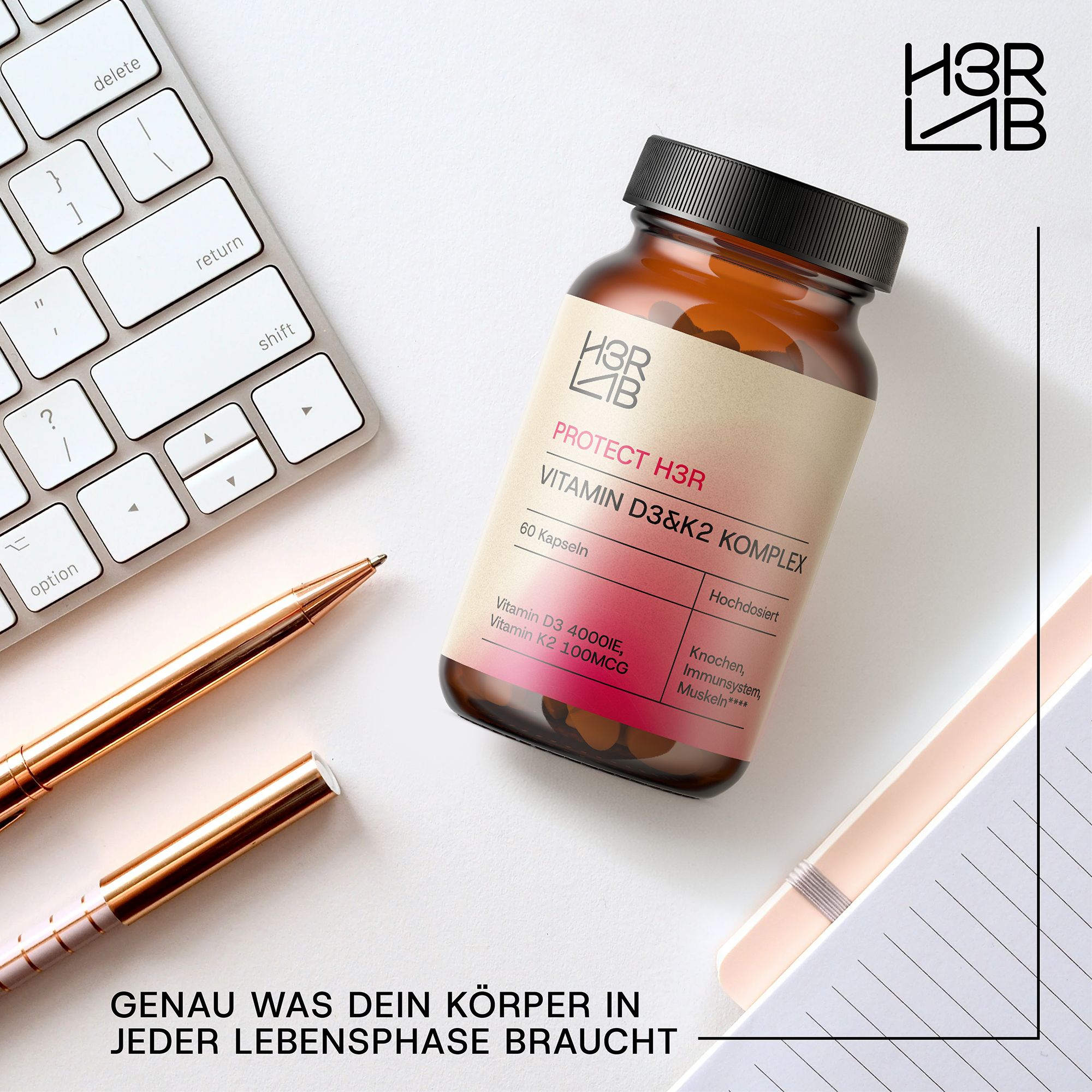 Braune Flasche mit Kapseln auf Schreibtisch. Etikett: Vitamin D3 & K2 Komplex. 60 Kapseln. Hochdosiert. Stifte und Notizbuch daneben.
