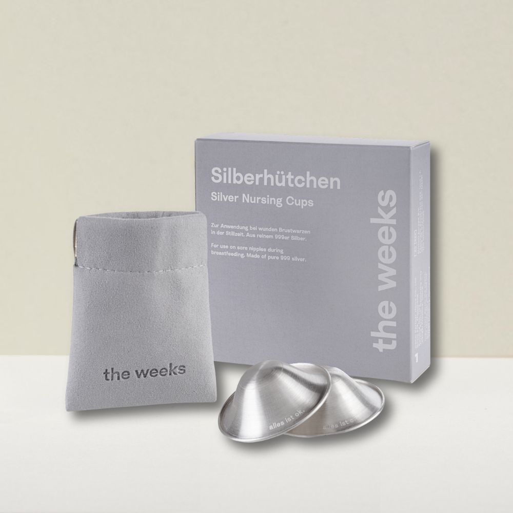 Zwei silberne Stillhütchen, graue Box und Beutel. Auf der Box steht "Silberhütchen" und "the weeks".