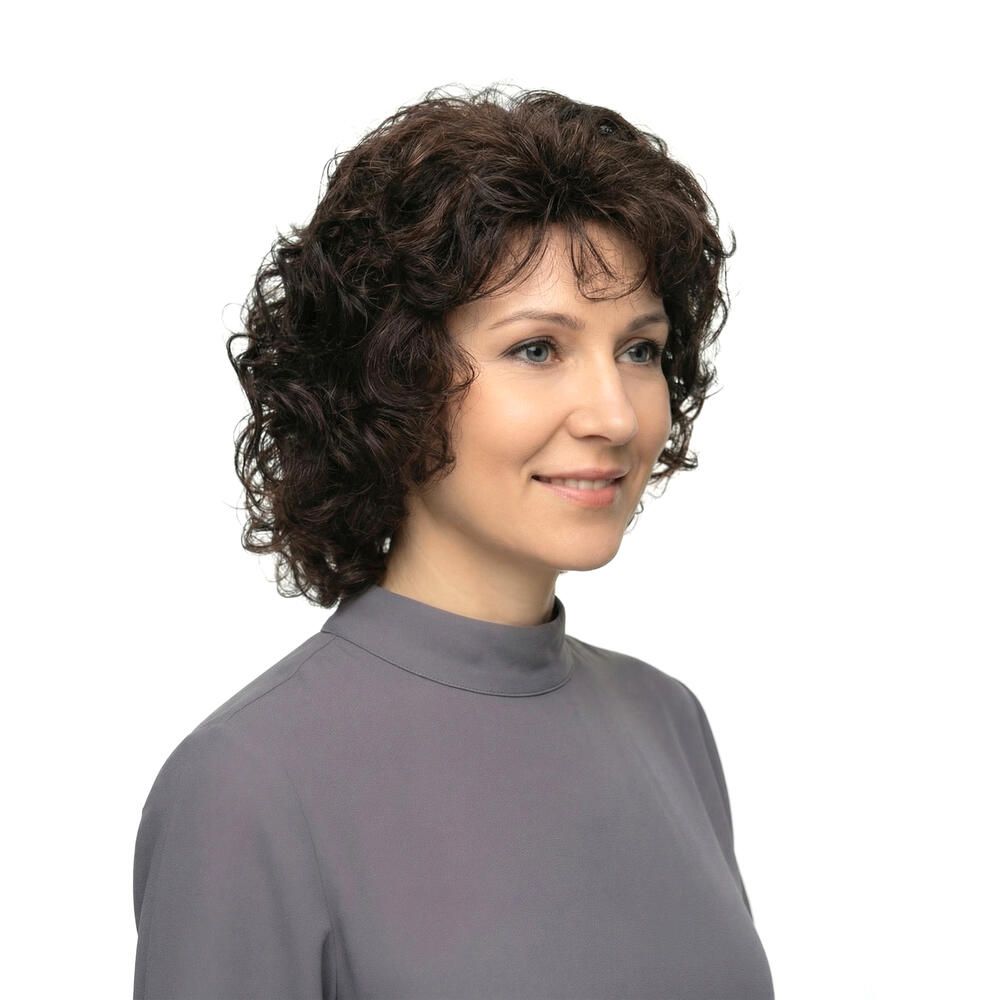 Frau mit brauner, lockiger Perücke. Nahaufnahme, lächelnd. Graues Oberteil.