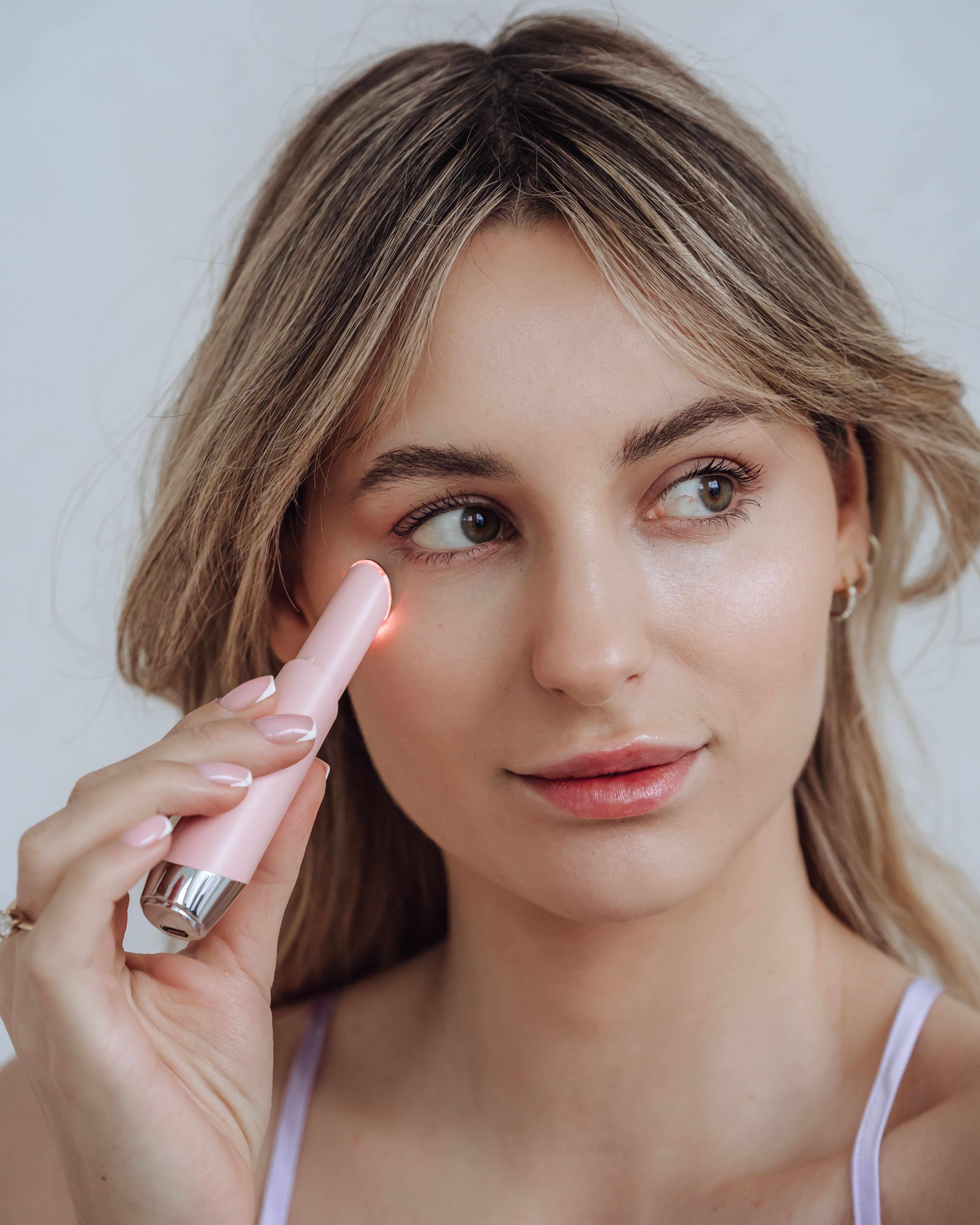 Frau hält rosa Gerät am Auge. Rotes Licht sichtbar. LED-Lichttherapiegerät.