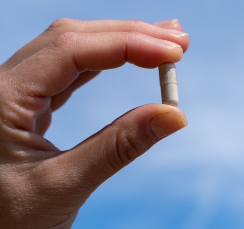 Finger hält eine einzelne Aavalabs Ashwagandha Kapsel vor blauem Himmel.