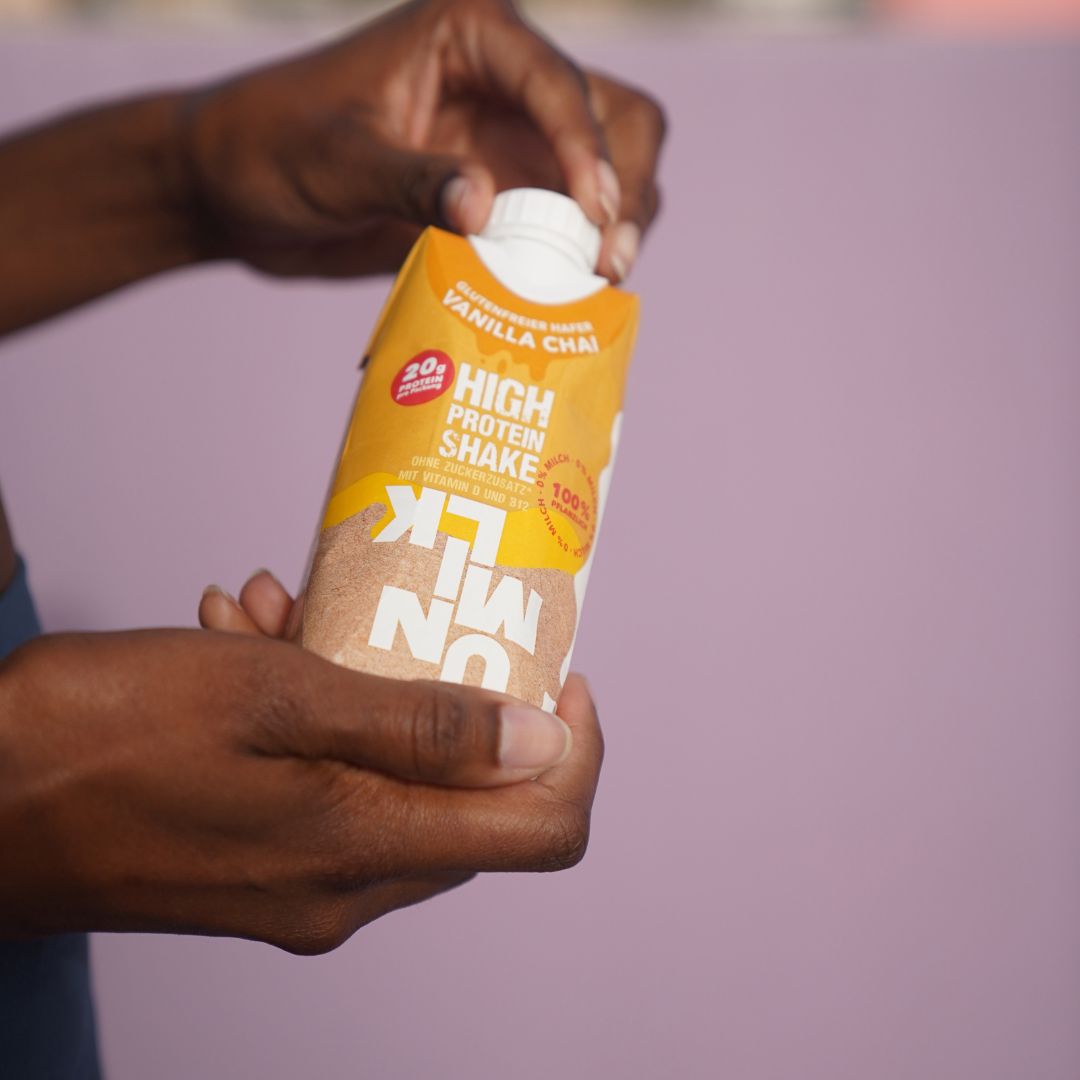 Hände halten UNMILK High Protein Shake Vanilla Chai. Aufschrift: 20g Protein, glutenfrei, 100% pflanzlich.