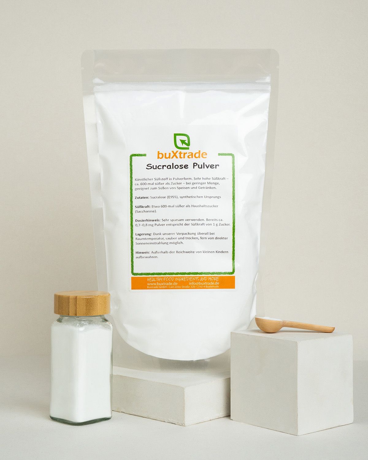 Buxtrade Sucralose Pulver in einem weißen Standbodenbeutel, daneben ein Glas und ein Holzlöffel.