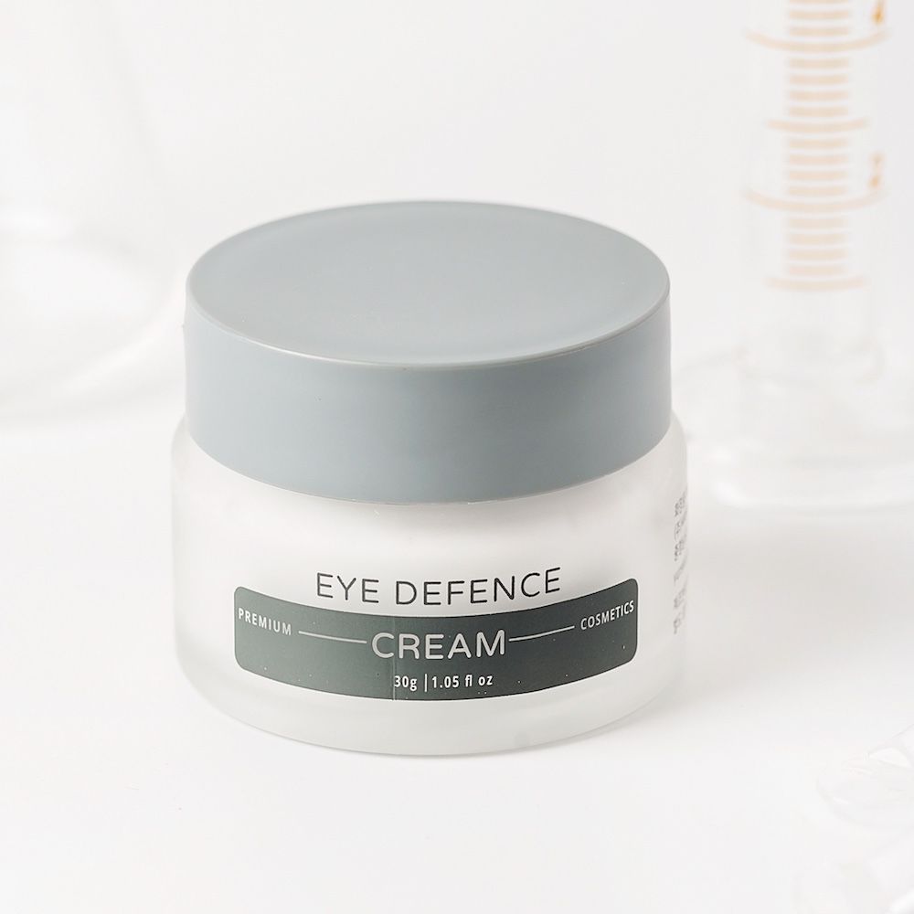 Glas mit grauen Deckel. Aufschrift: Eye Defence Cream. Hintergrund: Laborutensilien.