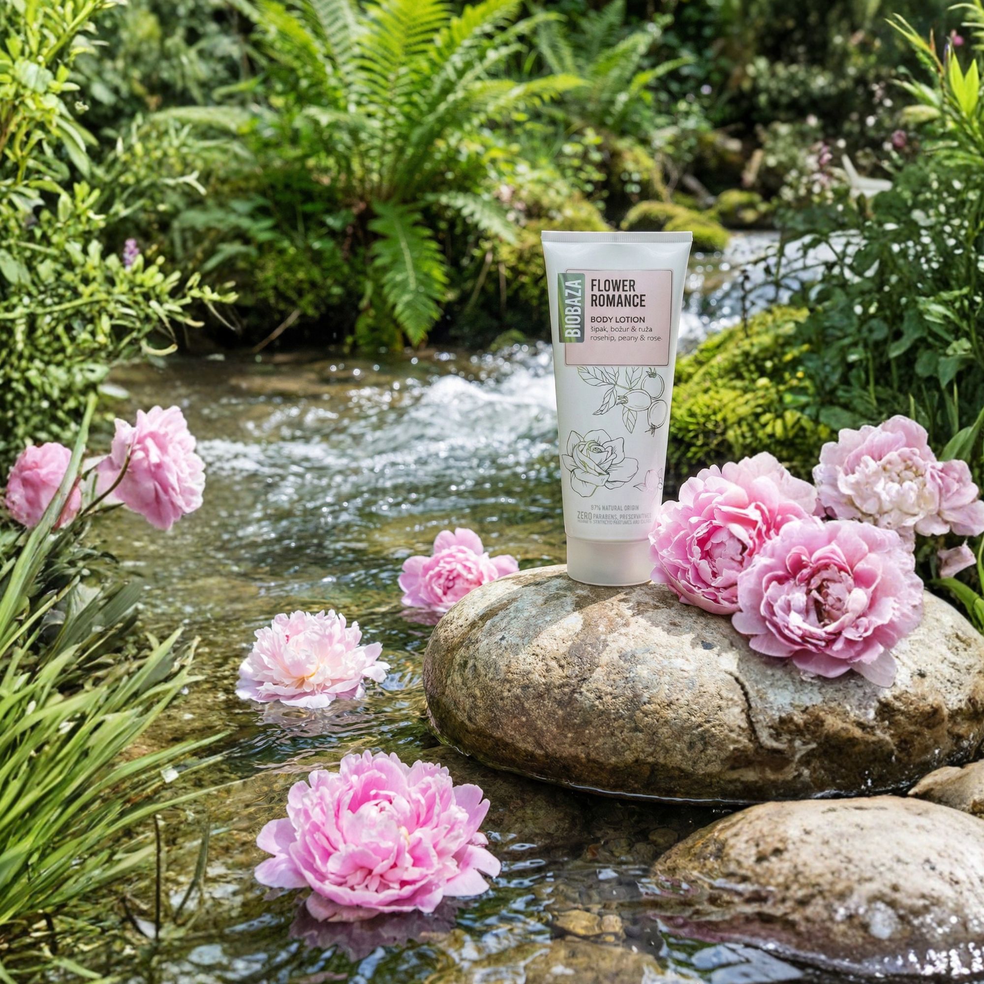 Biobaza Body Lotion Flower Romance Tube auf Stein im Bach, umgeben von rosa Blüten und grünen Pflanzen.