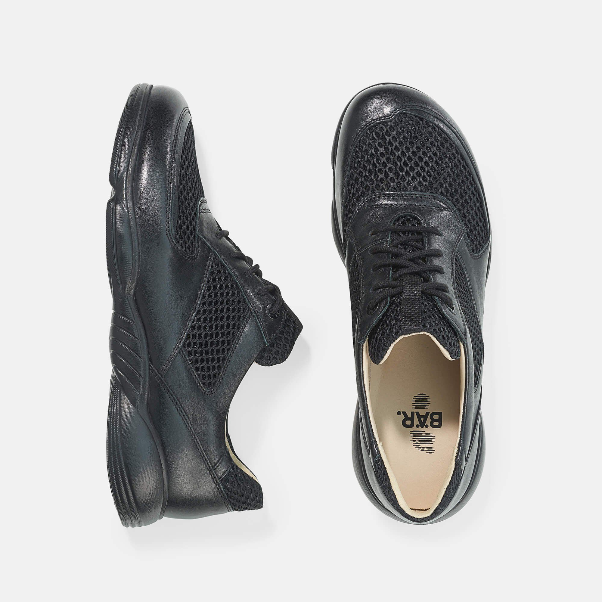 Zwei schwarze Schnürschuhe mit Mesh-Einsätzen. Breite Passform. Leder und Textil. Hellgrauer Hintergrund. Blick von oben.