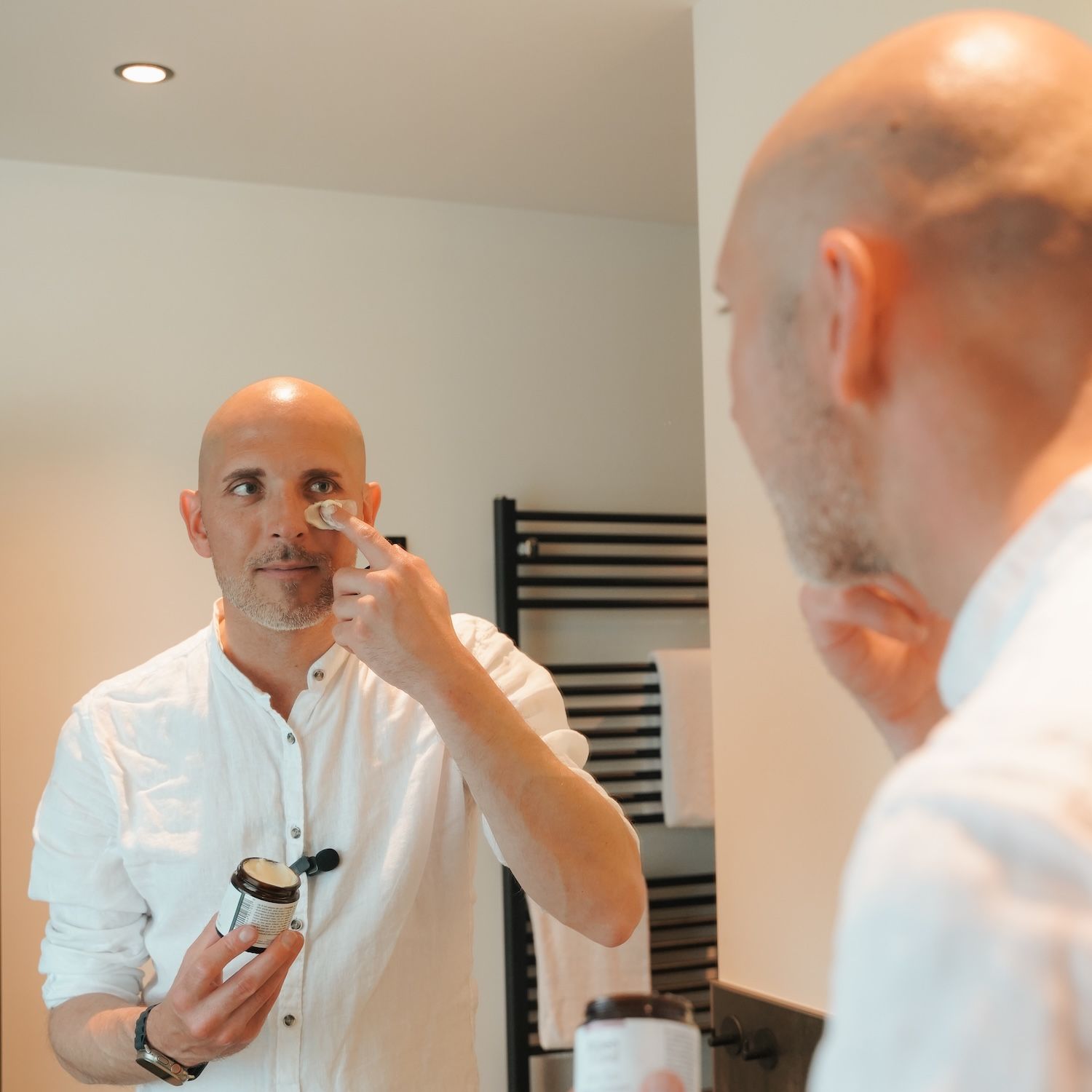 Mann im Spiegel, trägt AlpenXund After Sun Intensivbalsam auf. Dose und Deckel in der Hand.