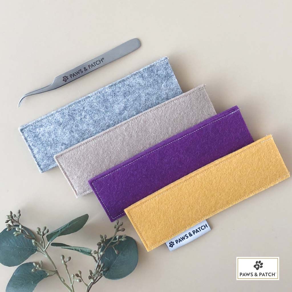 Zeckenpinzette und Etuis aus Filz in Gelb, Grau, Beige und Lila. Marke PAWS&PATCH. Aufschrift auf Etui.