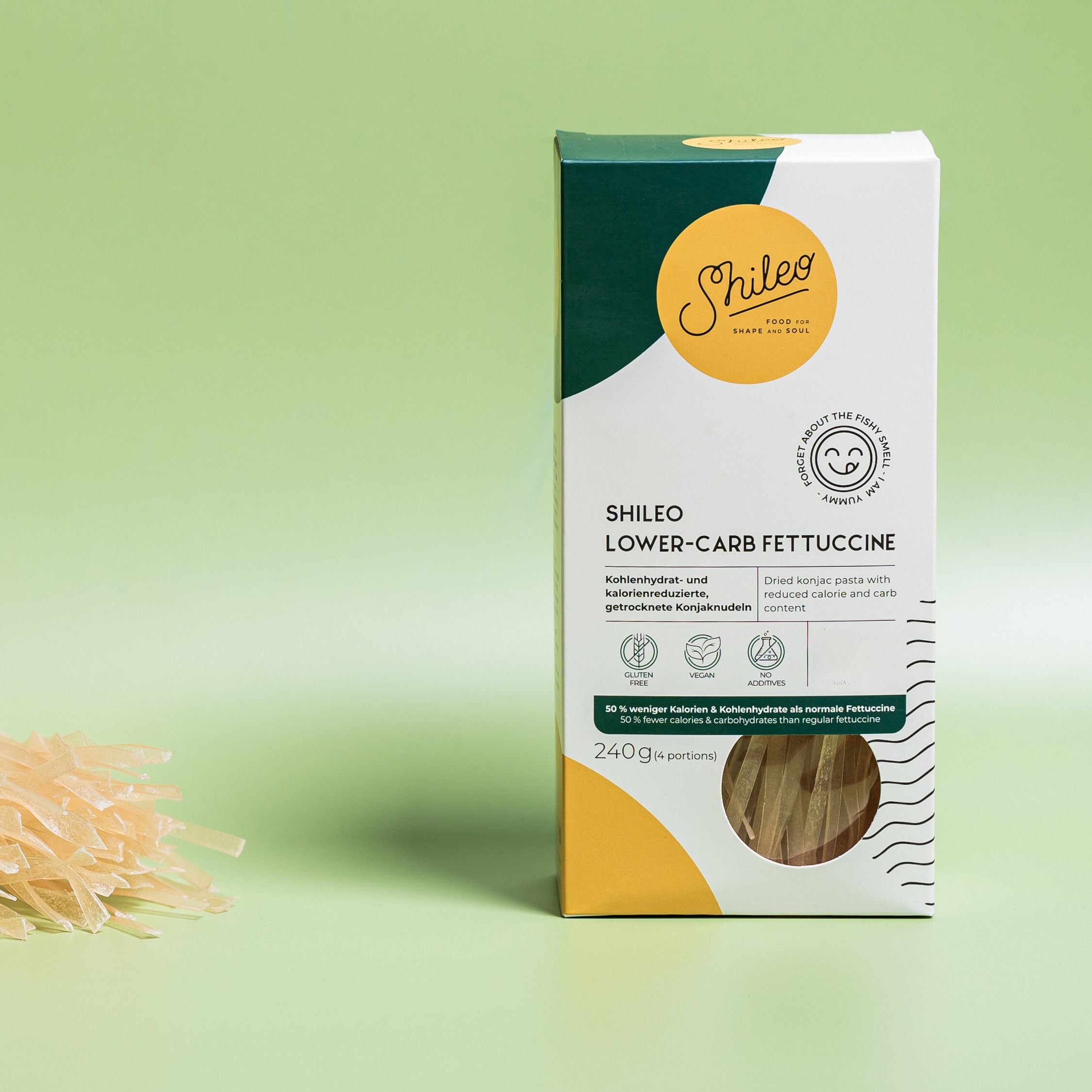Verpackung SHILEO Lower-Carb Fettuccine. Aufdrucke: Logo, Produktname, 240g. Nudeln liegen daneben. Grüner Hintergrund.