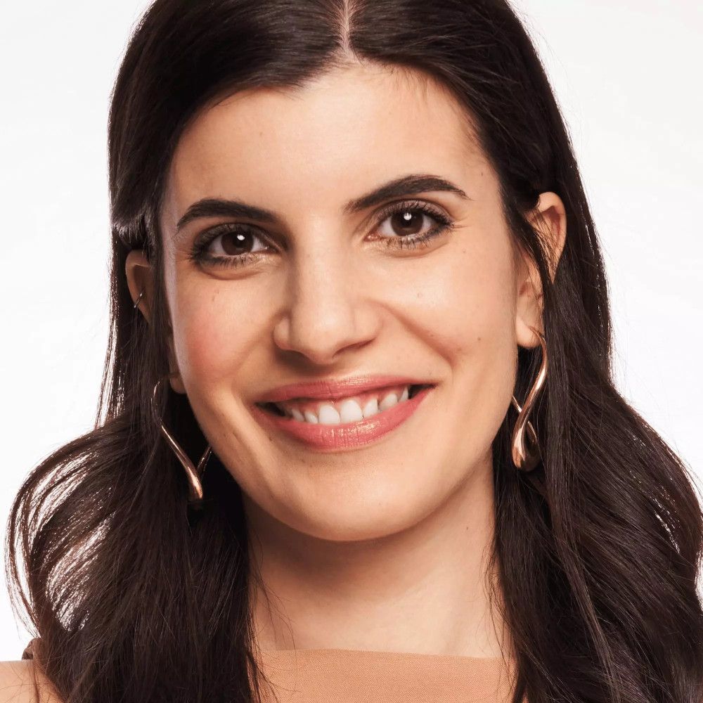 Porträt einer Frau mit dunklen Haaren und goldenen Ohrringen. Sie trägt Foundation.