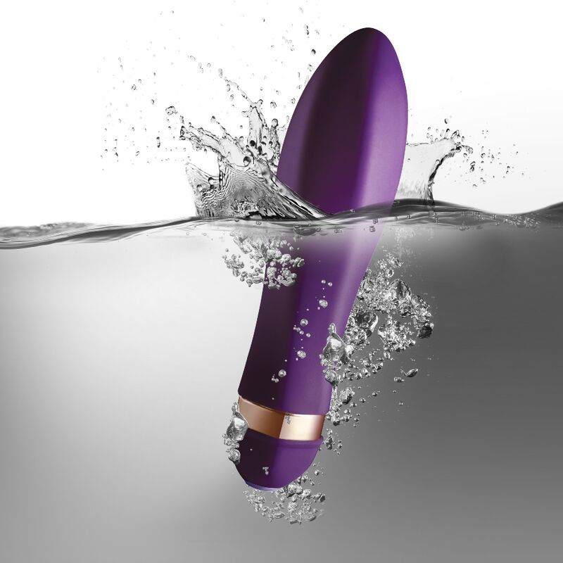 Lila Vibrator im Wasser, umgeben von Wasserspritzern. Goldfarbener Ring am unteren Ende.