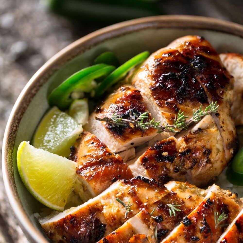 Gegrilltes Hähnchenbrustfilet, geschnitten. Garniert mit Limettenspalten und Kräutern. Nahaufnahme.