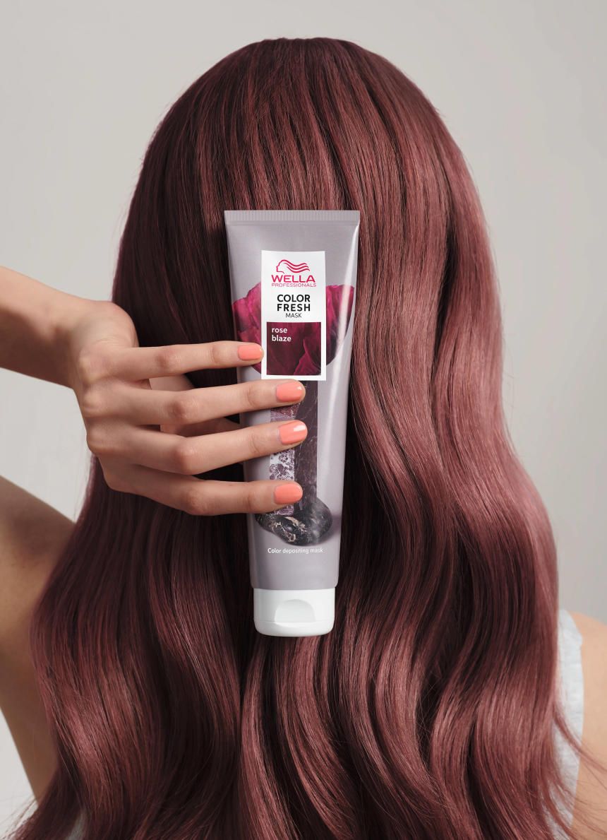 Person hält die Wella Color Fresh Mask Rose Blaze Tube vor gefärbtem Haar. Helle Haut und farbige Nägel.