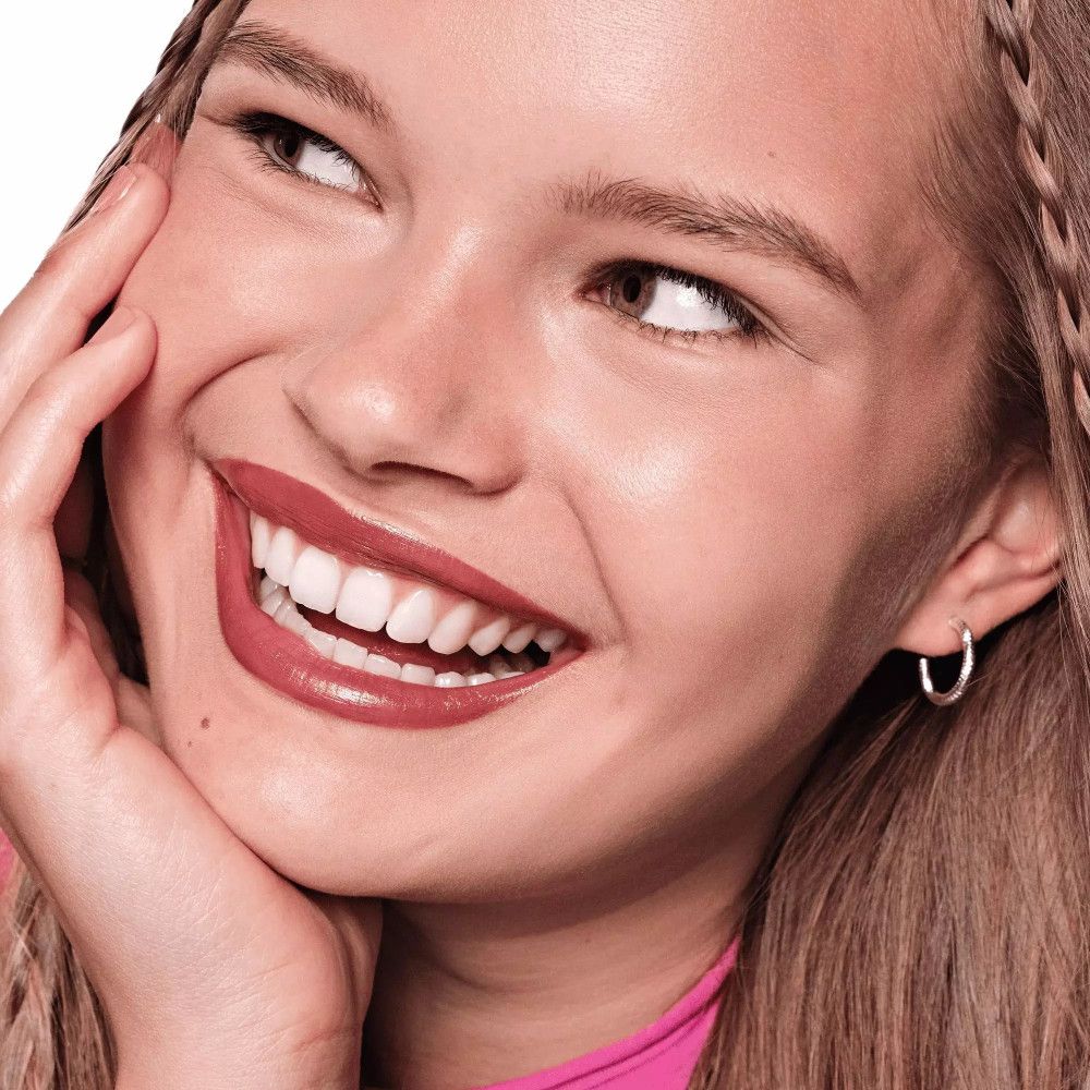 Porträt einer lächelnden Frau mit Lippenstift. Lippen in Rosé-Ton geschminkt. Frau berührt ihr Gesicht.