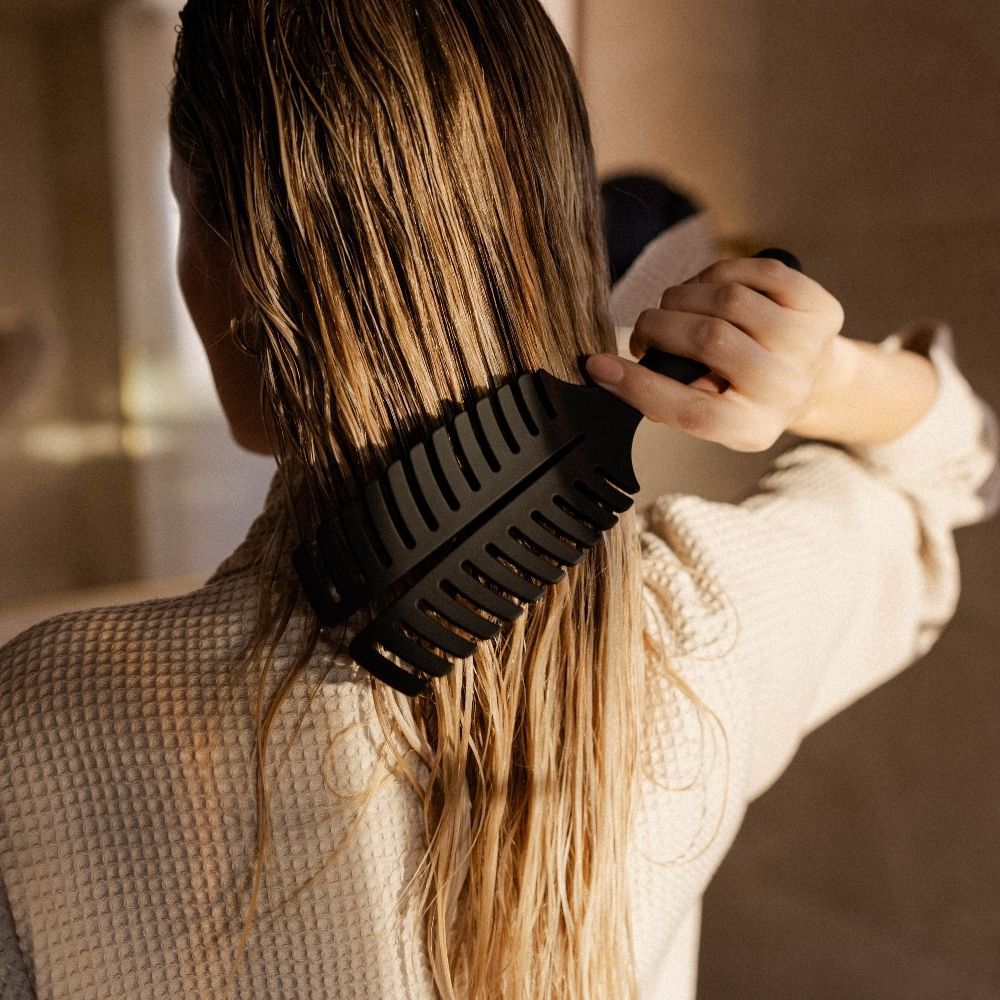 Frau bürstet sich mit schwarzer Haarbürste die nassen Haare.