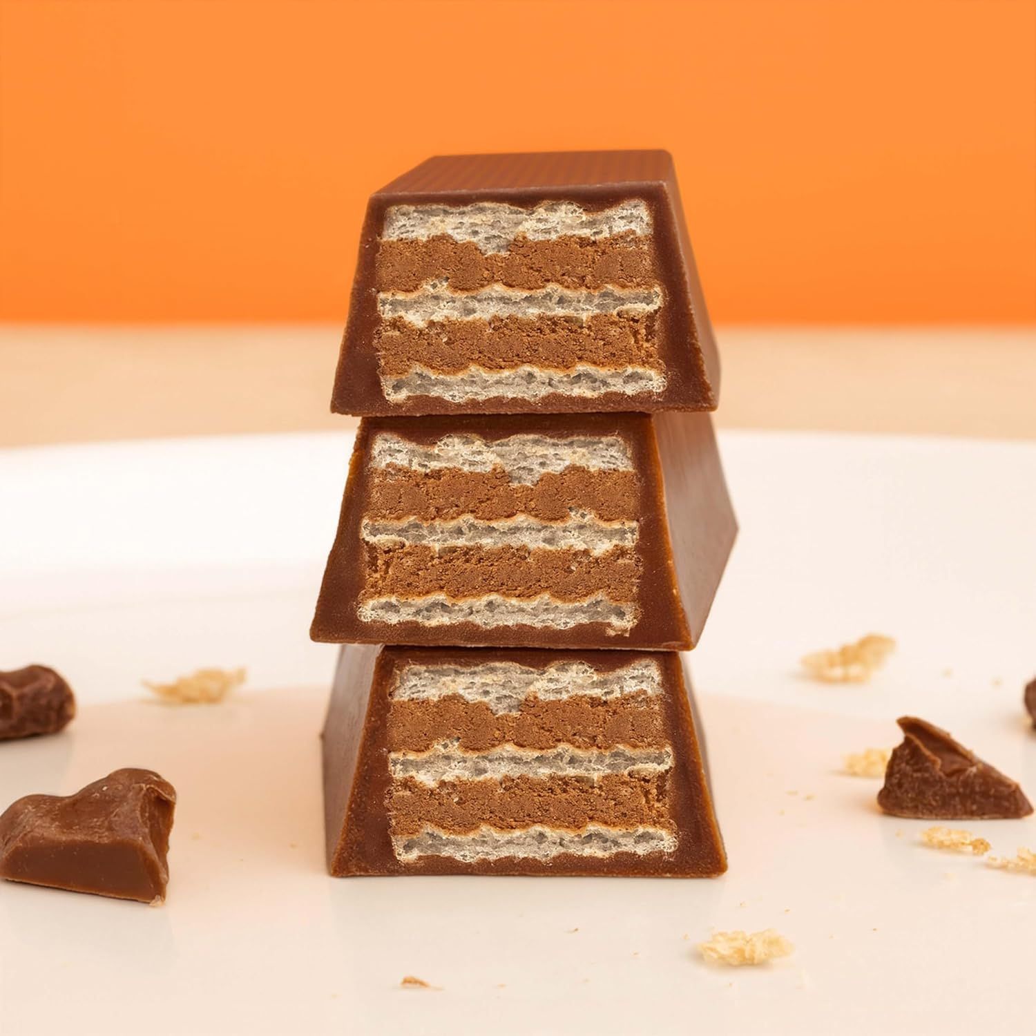 Drei gestapelte Schokoriegel mit Waffelschichten. Einzelne Schokostücke und Waffelstückchen liegen verstreut.