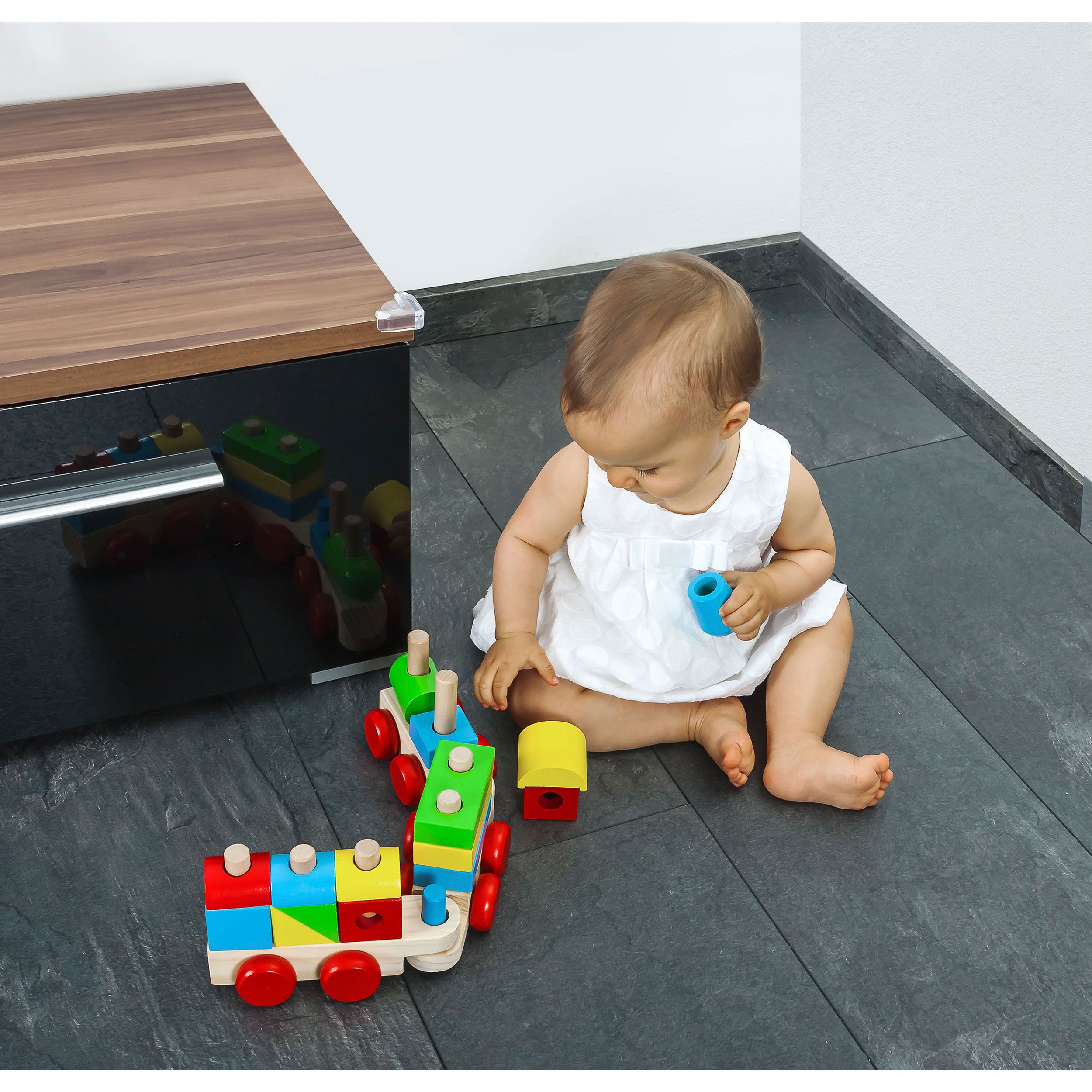 Baby spielt mit einem bunten Holzspielzeugzug. Der Zug besteht aus mehreren Waggons mit verschiedenen Holzbausteinen.