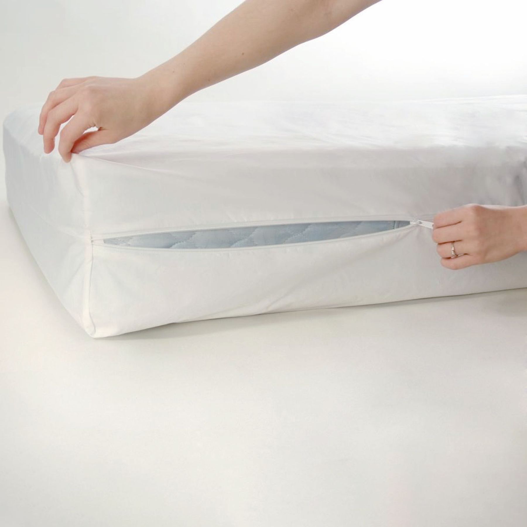 Weißer Matratzenbezug mit Reißverschluss. Eine Hand öffnet den Reißverschluss.