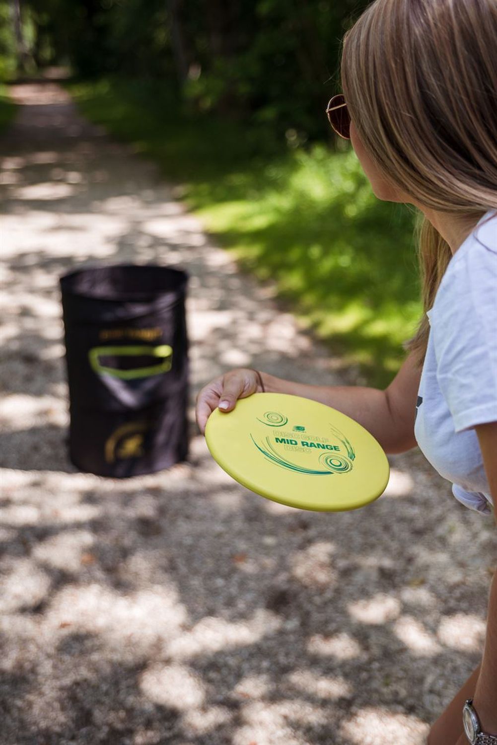 Person hält gelbe Disc Golf Scheibe (Mid Range) in der Hand. Person steht auf einem Kiesweg.