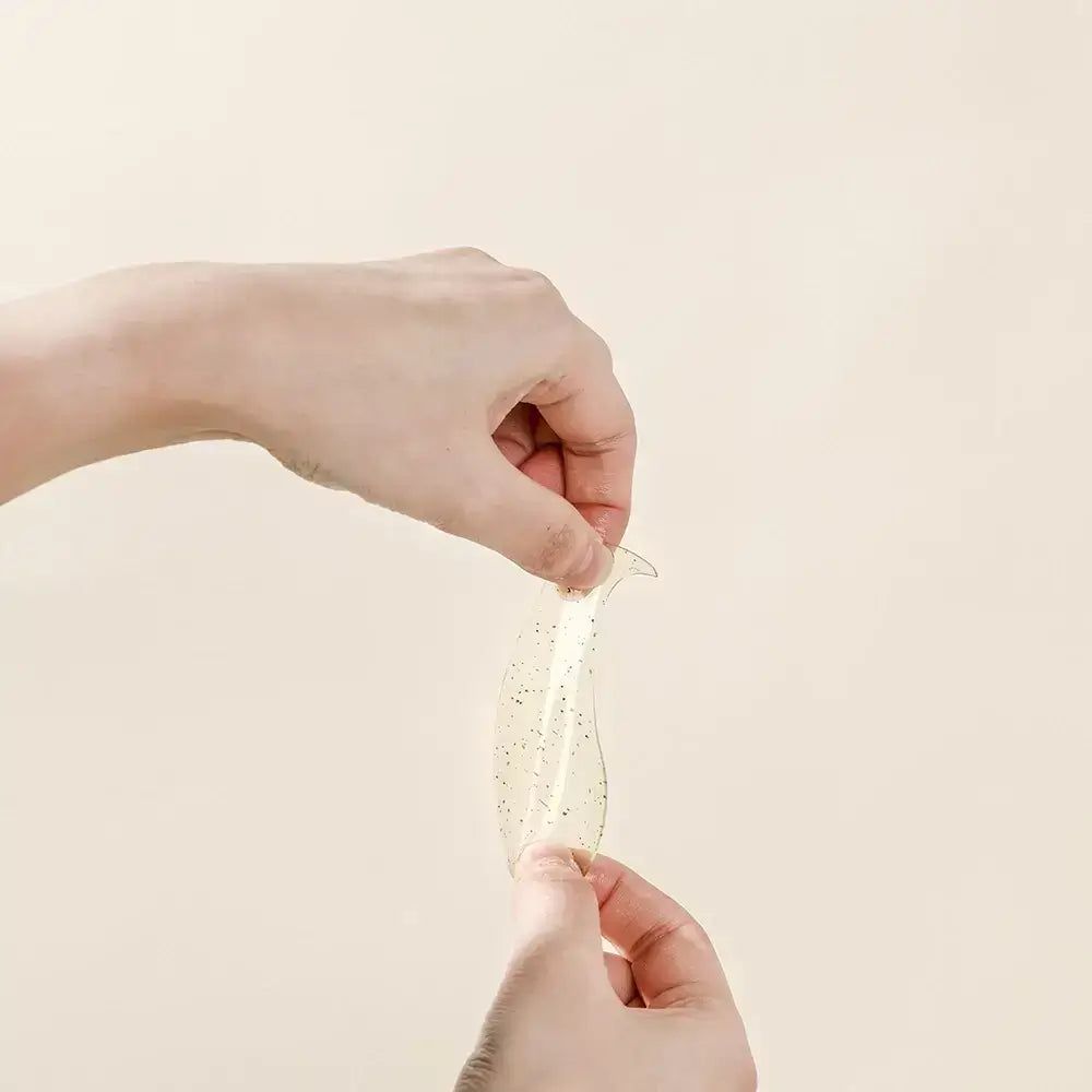 Hände halten ein Augen-Gel-Pad. Transparentes Pad mit kleinen schwarzen Punkten. Form: gebogen.