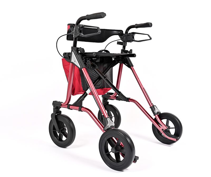 Rot-schwarzer Rollator mit vier Rädern. Er hat einen Korb, eine Rückenlehne und Handgriffe. Der Rahmen ist rot.