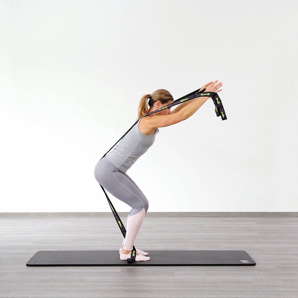 Frau trainiert auf einer Matte mit einem schwarzen Elastikband. Das Band ist an Händen und Füßen befestigt.