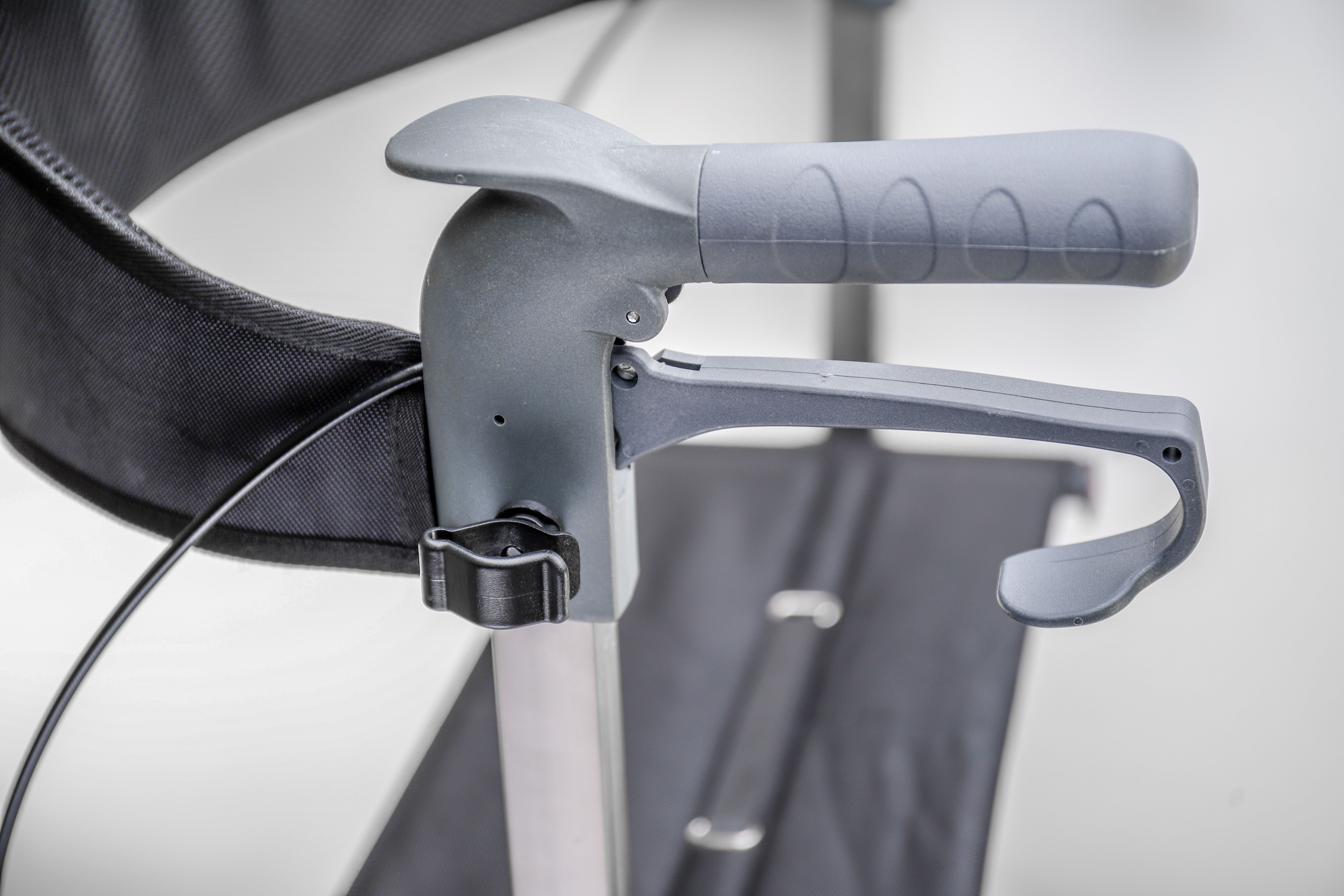 Rollator-Griff mit Bremshebel. Graue Farbe. Schwarzer Gurt. Detailaufnahme.