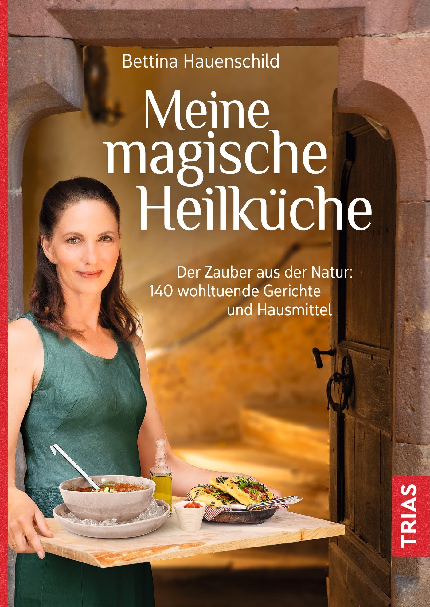 Buchcover mit Titel "Meine magische Heilküche" von Bettina Hauenschild. Frau hält Tablett mit Essen. TRIAS-Logo.