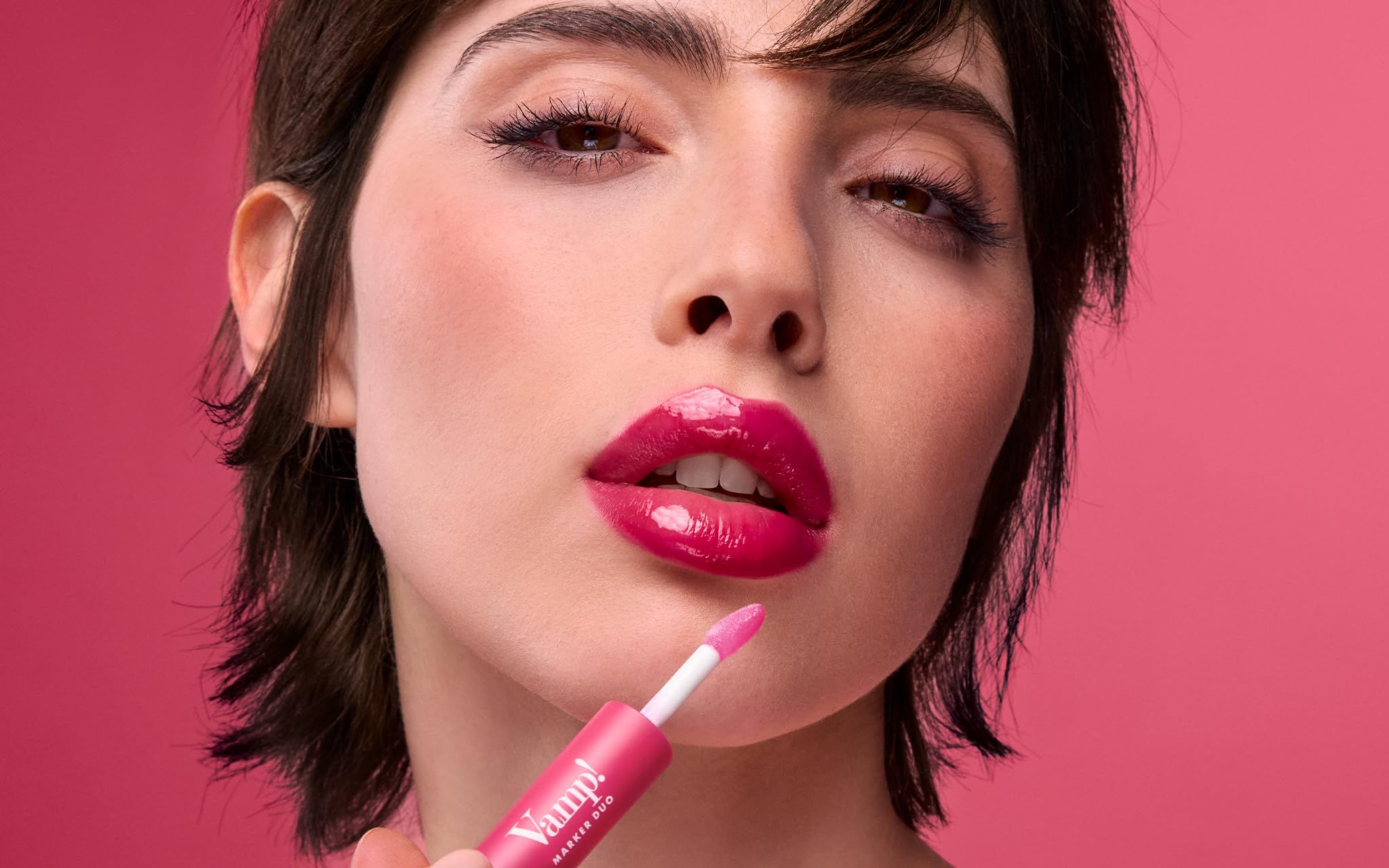 Frau mit vollen Lippen, die einen glänzenden, pinken Lippenstift aufträgt. Der Applikator ist sichtbar.