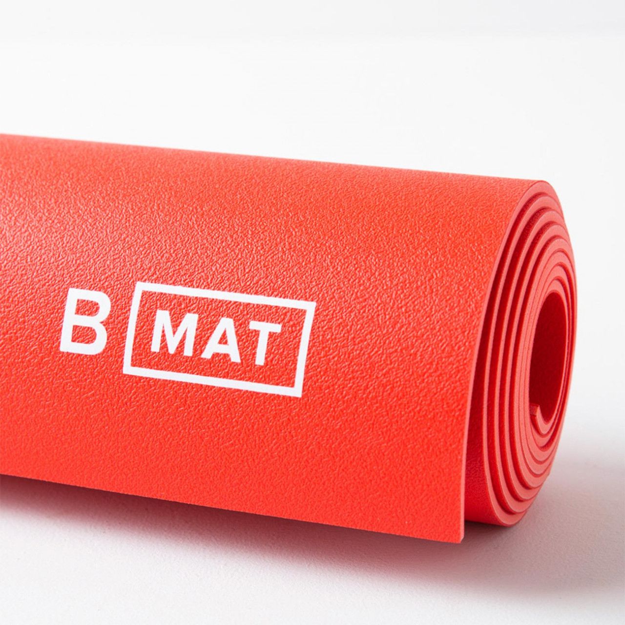 Gerolltes rotes Yogamatten-Detail. Logo B MAT, weiß. Sichtbare Rollenstruktur.
