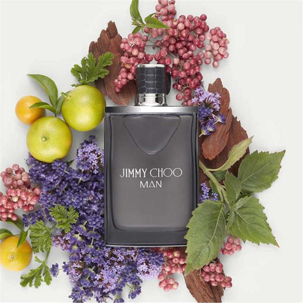Jimmy Choo Man Eau de Toilette-Flakon, umgeben von Früchten, Blüten und Holz. Graue Flasche, silberner Deckel.