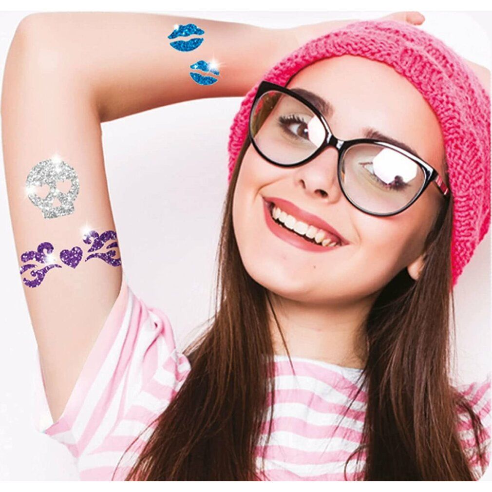Arm mit Glitzer-Tattoos: Kussmund, Herz-Flügel, Totenkopf. Person trägt Brille und Mütze.