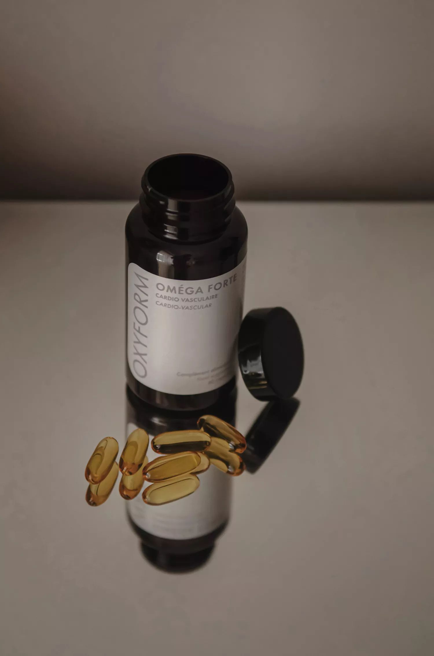 Braune Flasche mit geöffnetem Deckel und Kapseln daneben. Text: Oxyform, Oméga Forte, Cardio vasculaire.