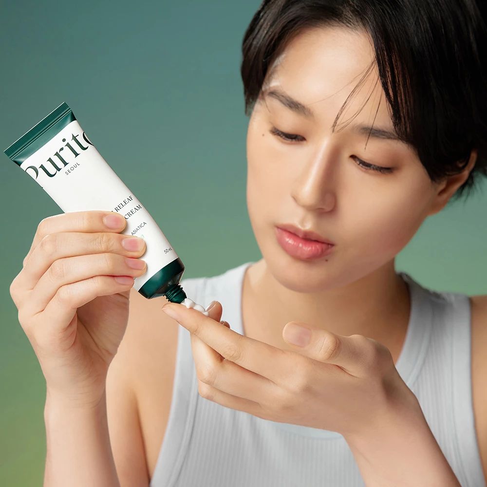 Frau drückt Creme aus Tube. Tube: PURITO, Wonder Releaf Cream. Creme auf Finger. Hintergrund: grün-blau.