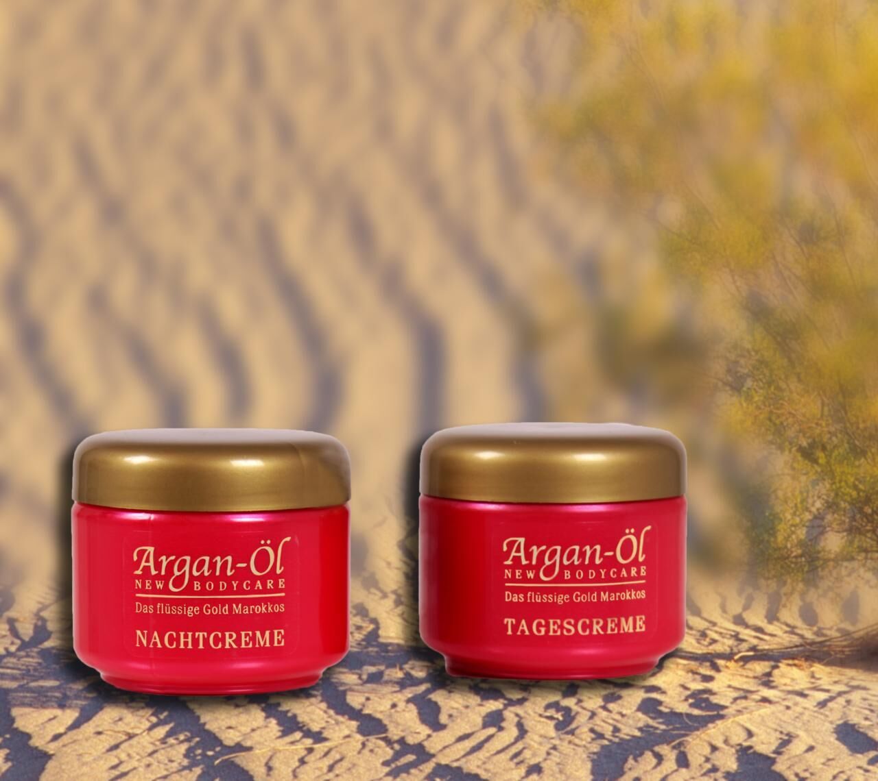 Zwei rote Tiegel mit goldenen Deckeln. Aufschrift: Argan-Öl, Nachtcreme und Tagescreme. Hintergrund: verschwommene Wüste.