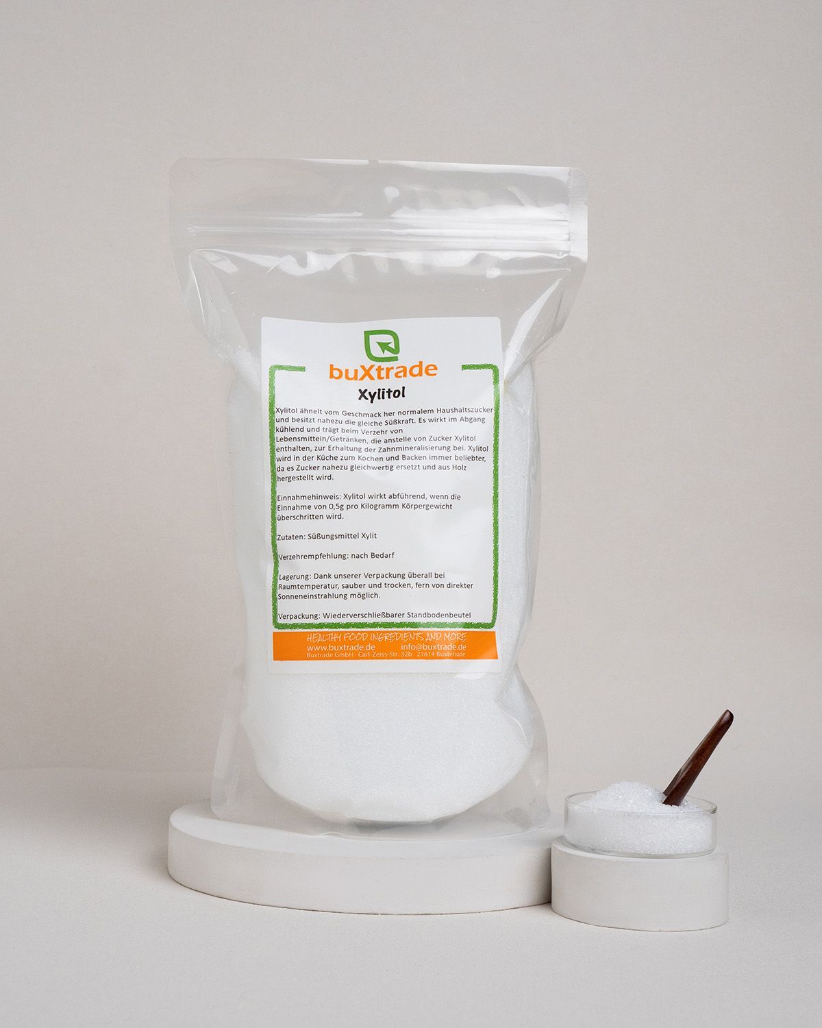 Transparente Verpackung mit Xylit. Etikett mit Produktinformationen und Logo 'buXtrade Xylitol'. Schale mit Xylit und Löffel.