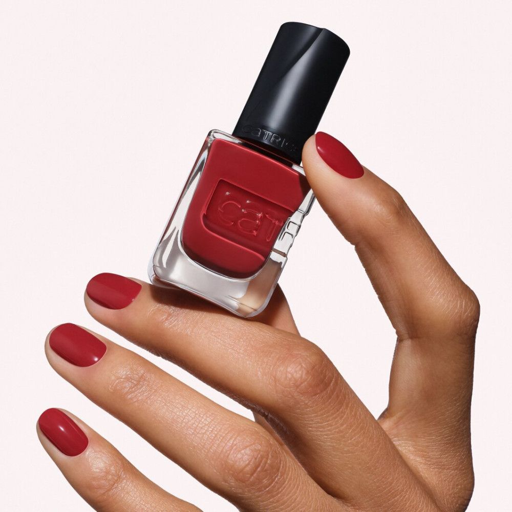 Rote Nagellackflasche mit schwarzem Deckel, gehalten von einer Hand mit lackierten Nägeln.