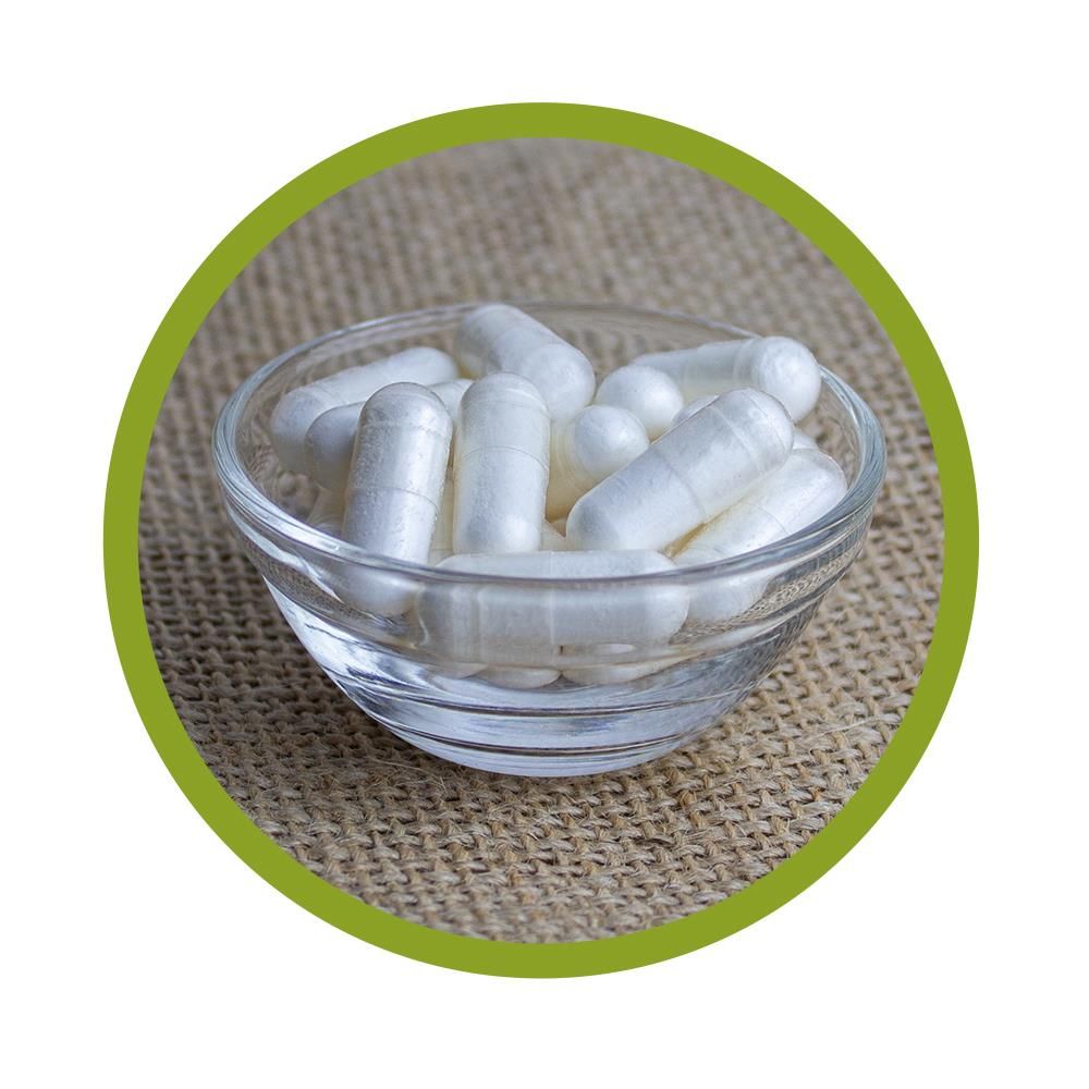 Klare Glasschale mit weißen Kapseln. Auf grobem Untergrund platziert.