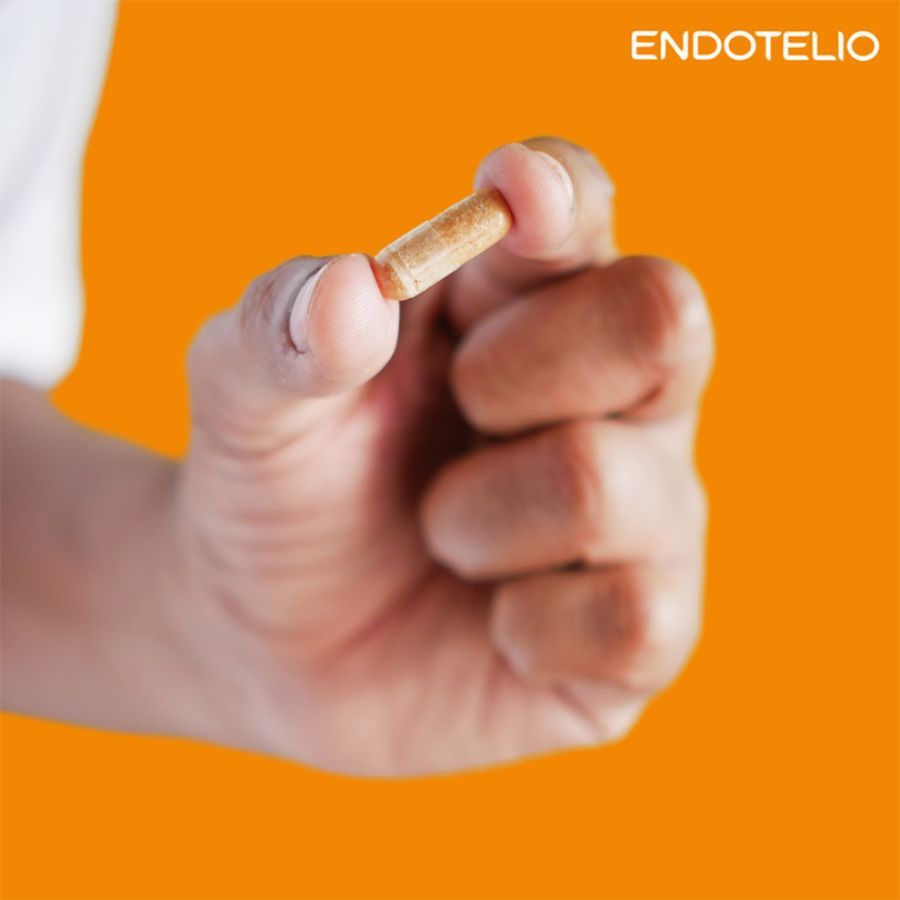 Hand hält eine einzelne Kapsel. Aufschrift: Endotelio. Hintergrund orange.