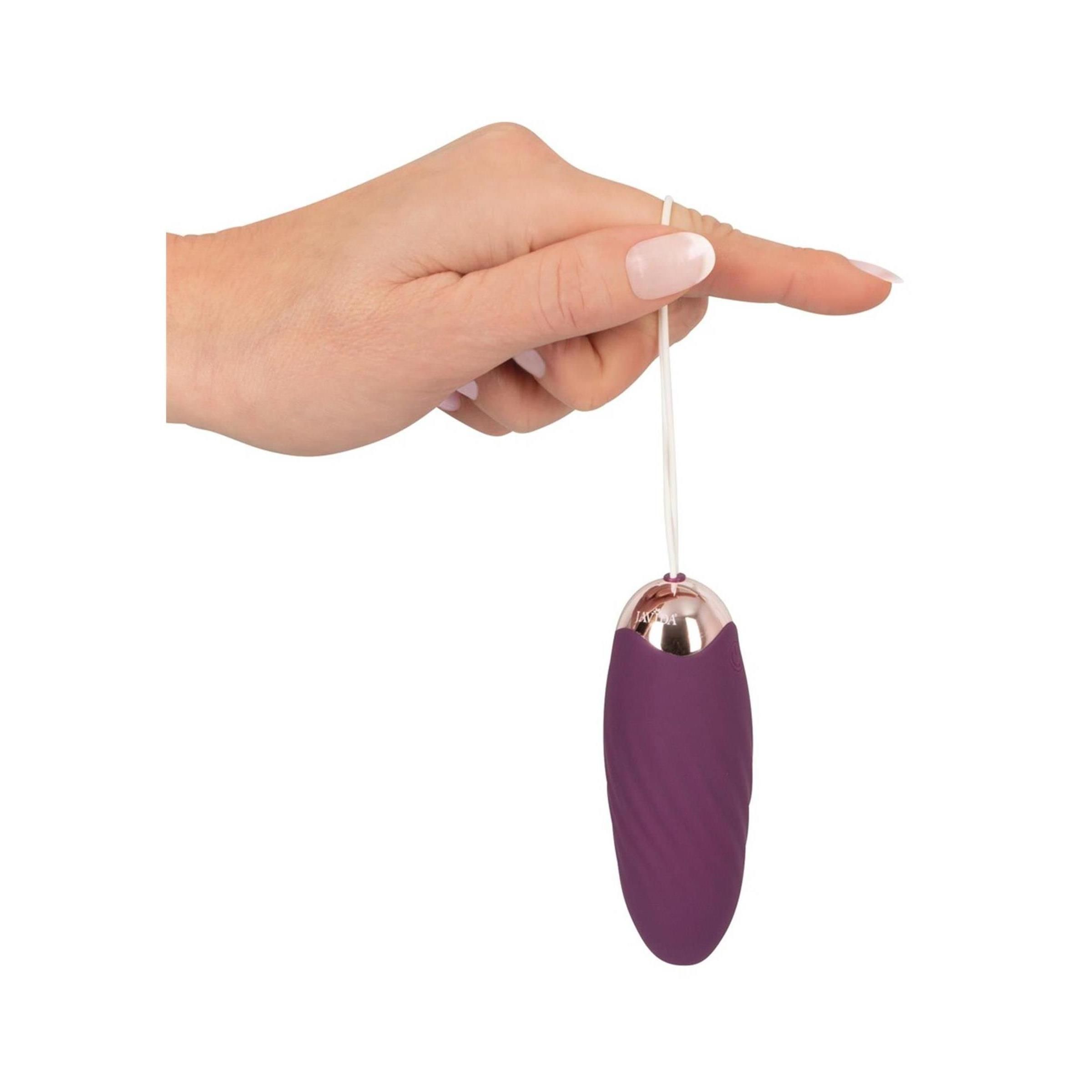 Javida Shaking Love Ball an Schnur, gehalten von Finger. Lila, oval, goldfarbener Abschluss.