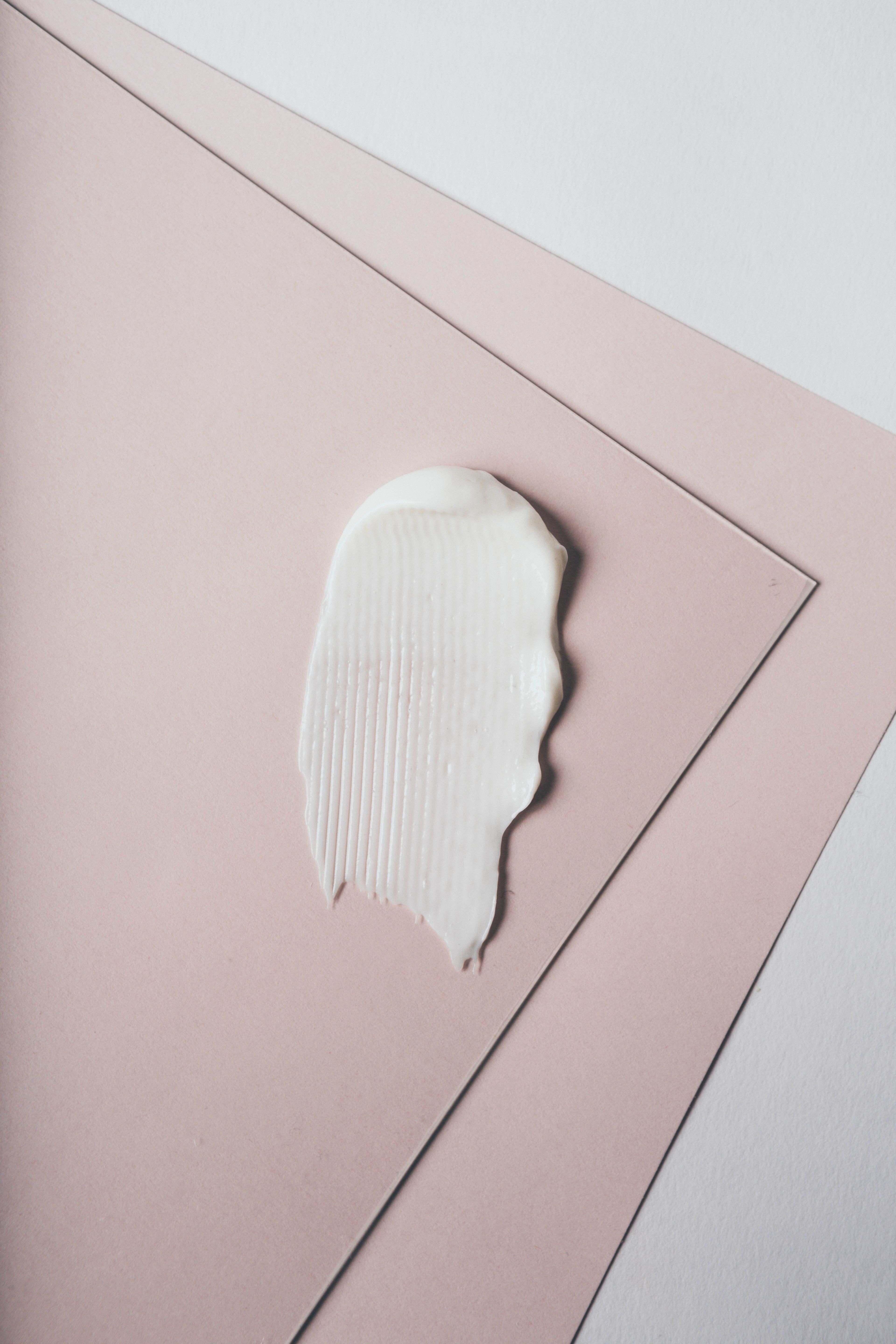 Weißer Cremekleck auf rosa Papier. Geriffelte Textur. Draufsicht.