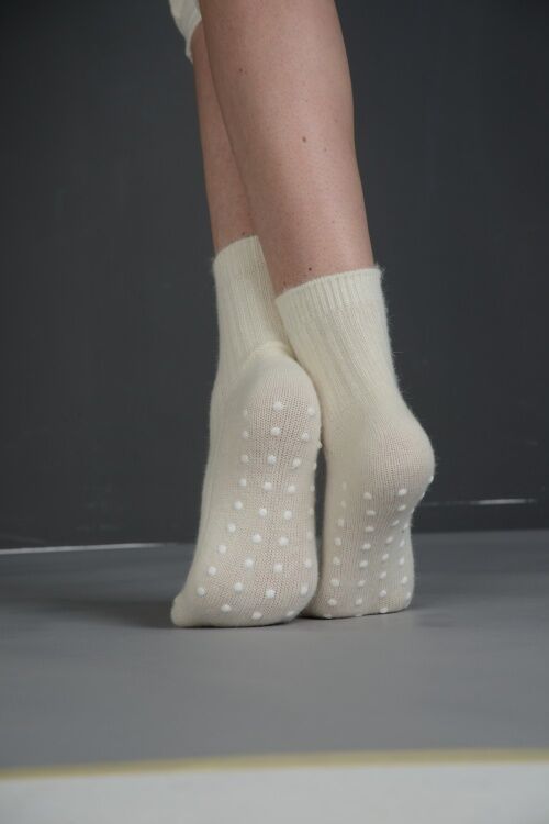 Beige Socken mit Anti-Rutsch-Noppen an der Sohle. Füße auf grauem Untergrund.