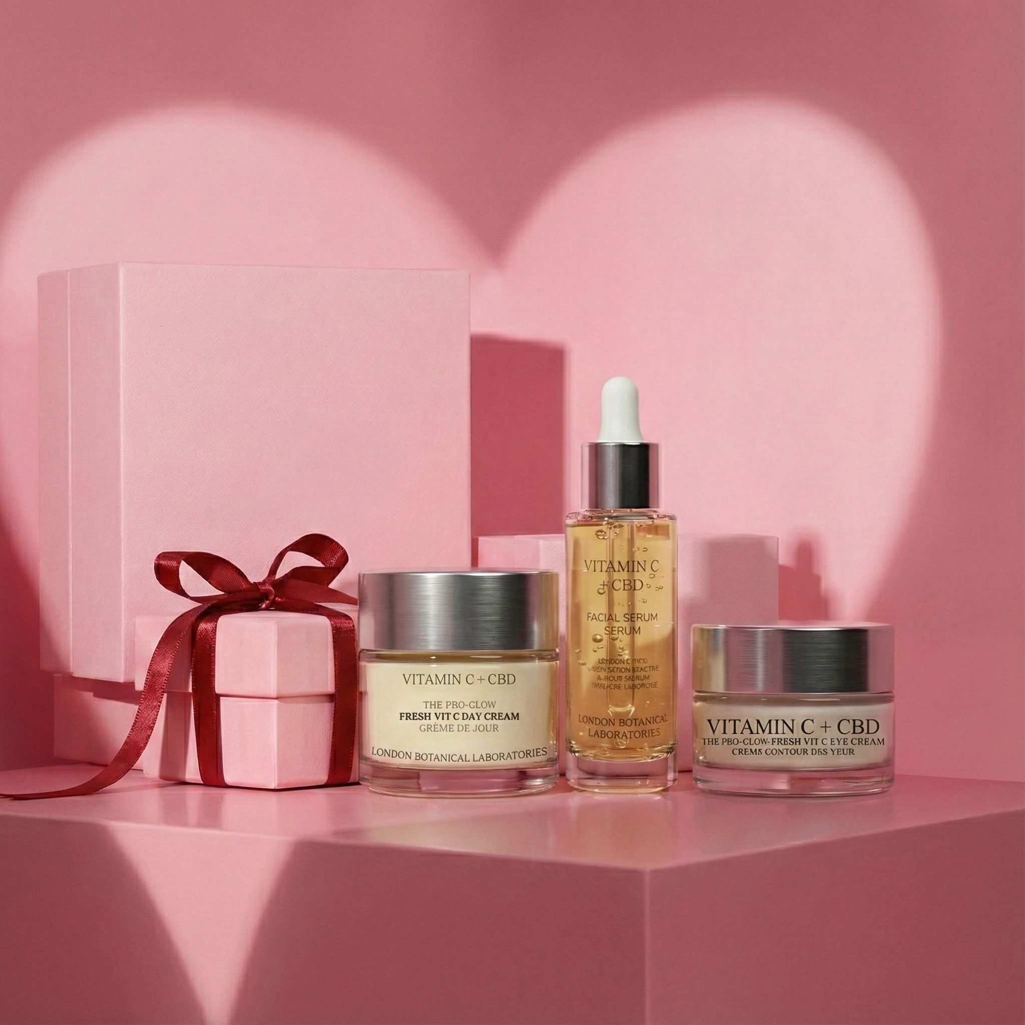Kosmetikprodukte auf rosa Podest. Tagescreme, Augencreme und Serum. Geschenkbox mit Schleife. Hintergrund: Herzform.
